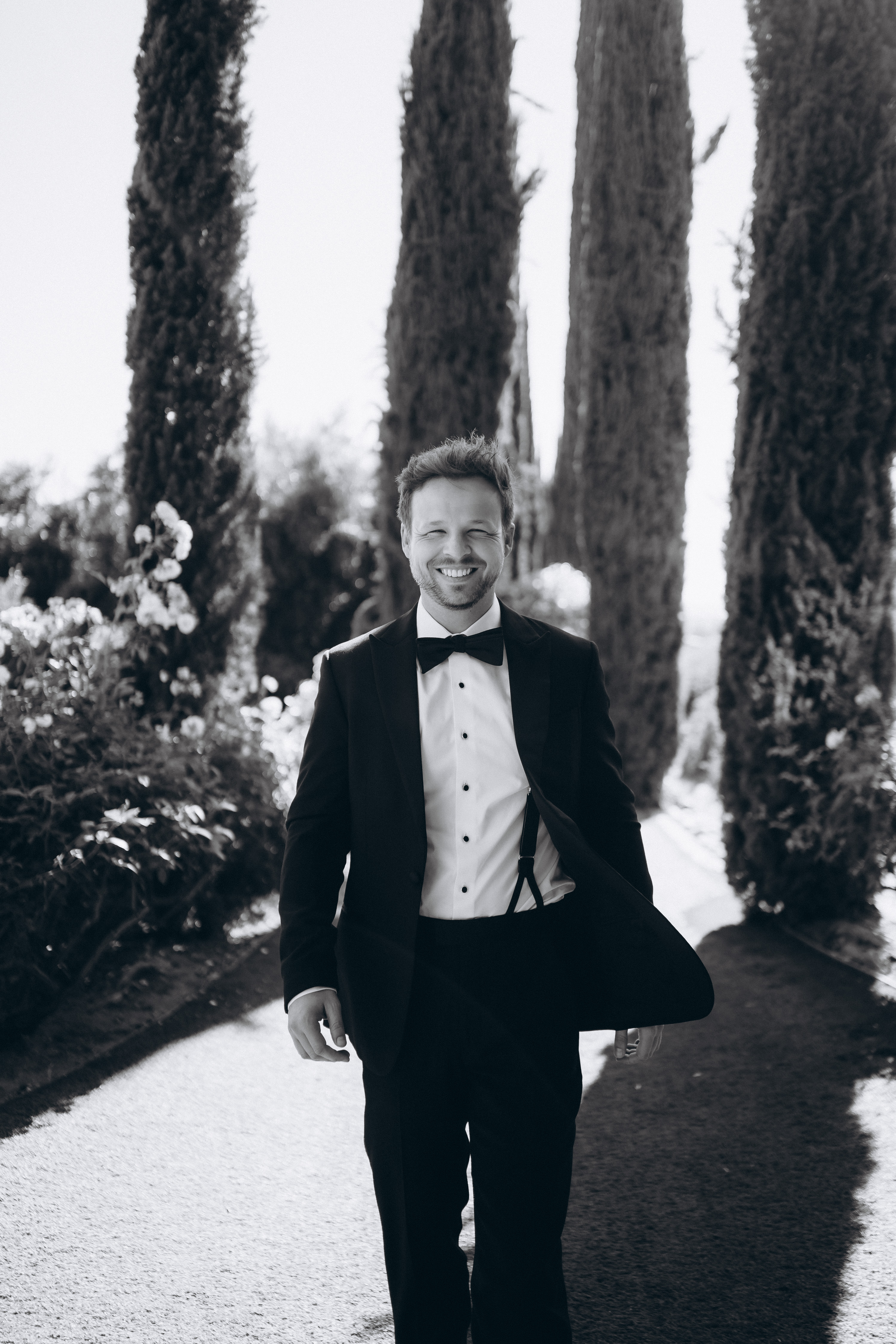 Groom in tuxedo between cypress trees
