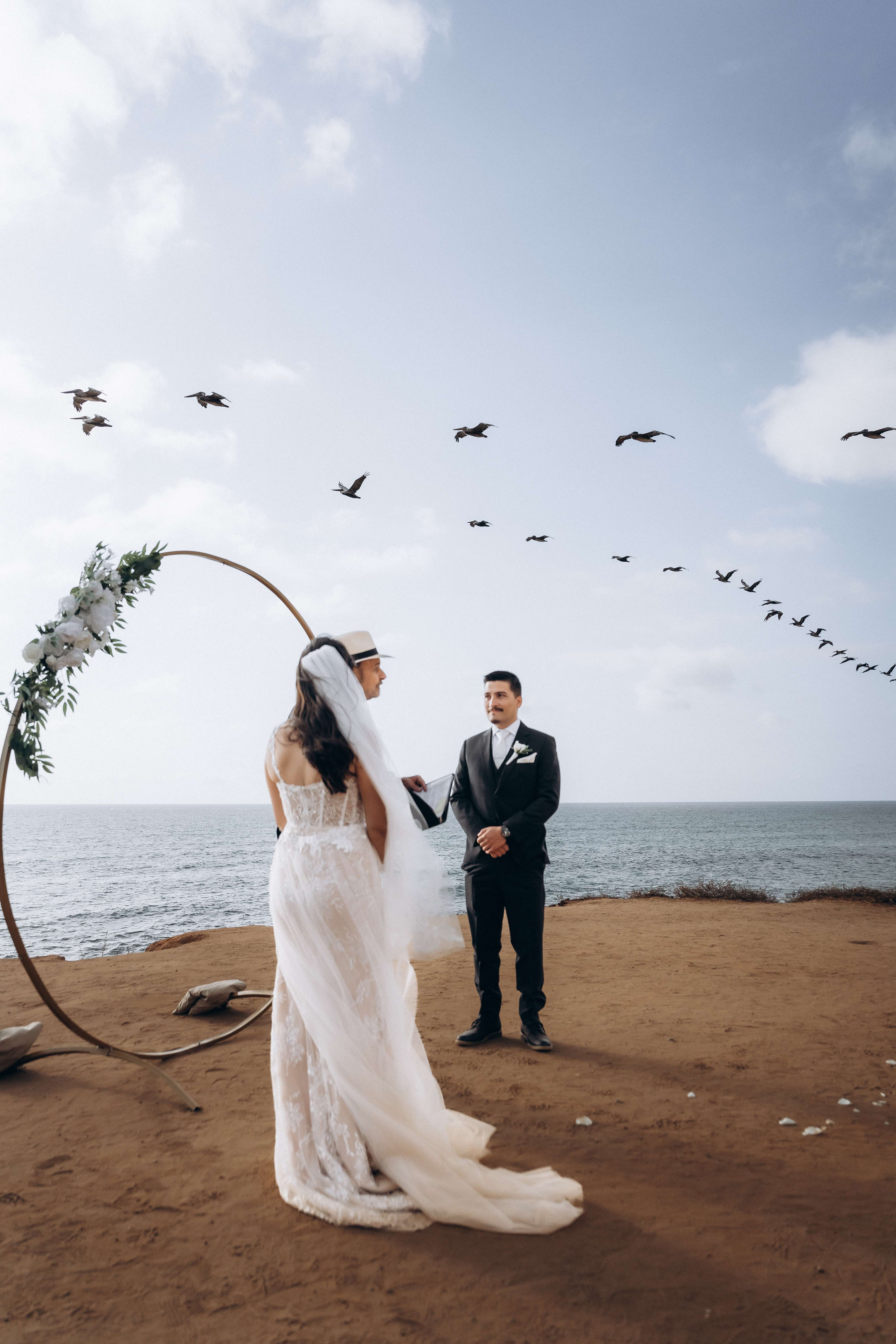 Beach wedding ceremony with birds in flight